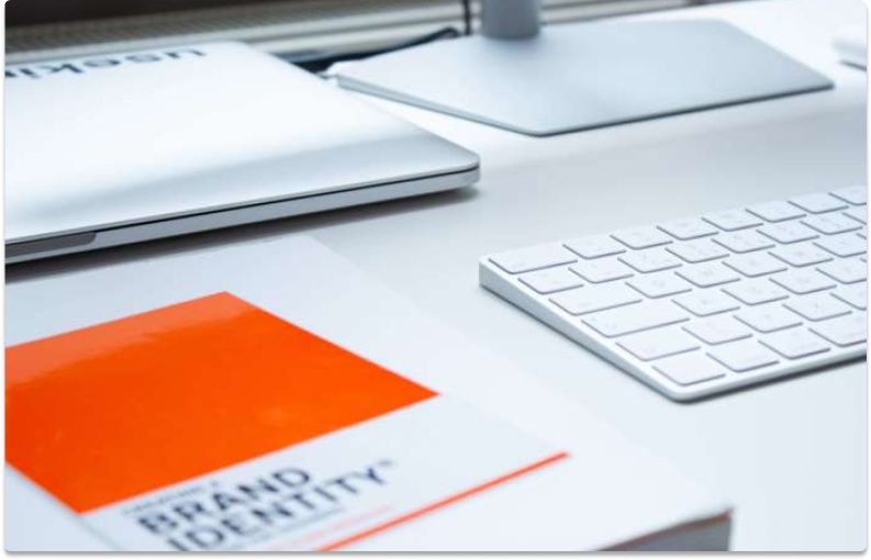 laptop, keyboard in background with brand design book in foreground